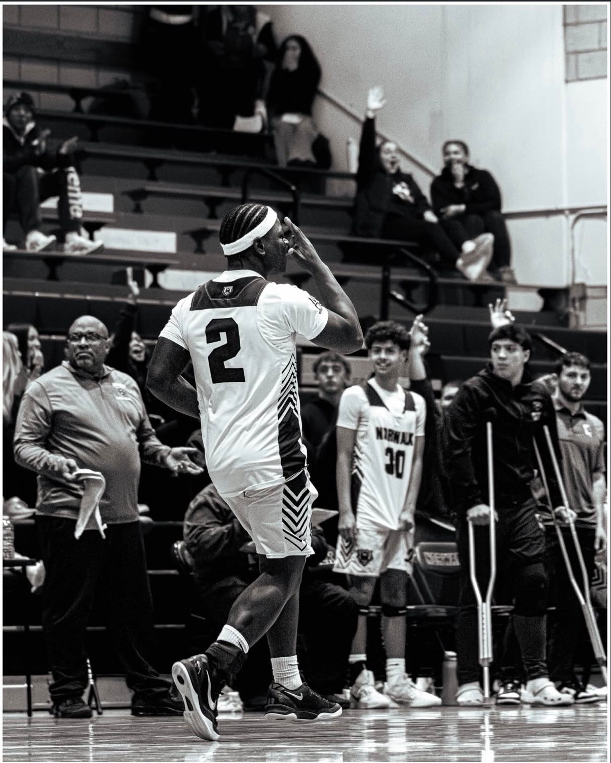 Black and white basketball photo of a player attacking the lane near the basket. The player is celebrating and running backwards after scoring 3. 