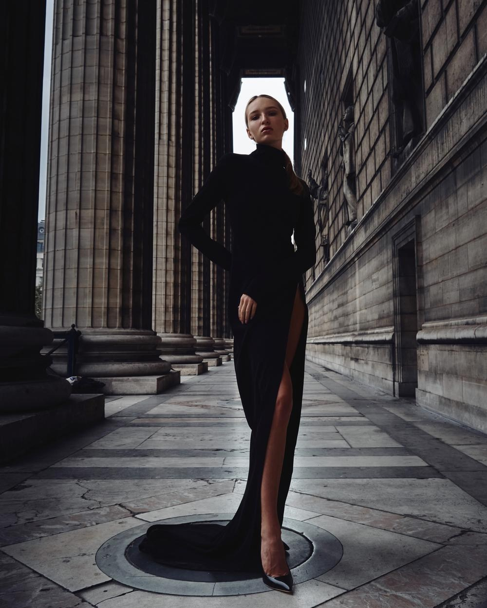 High-fashion campaign image with a high-slit black evening gown among classical columns