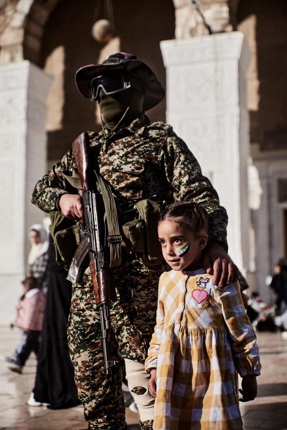 Damas (SYRIE), 16 décembre 2024 – Une fillette pose en compagnie d'un rebelle ayant participé à l'offensive conduisant à la chute de Bachar al-Assad, dans la cour de la Mosquée des Omeyyades, pour une photo historique.