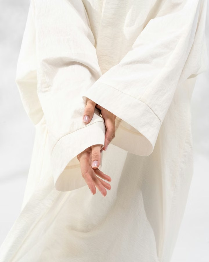 Fashion detail shot showing a model's hands emerging from wide white sleeves