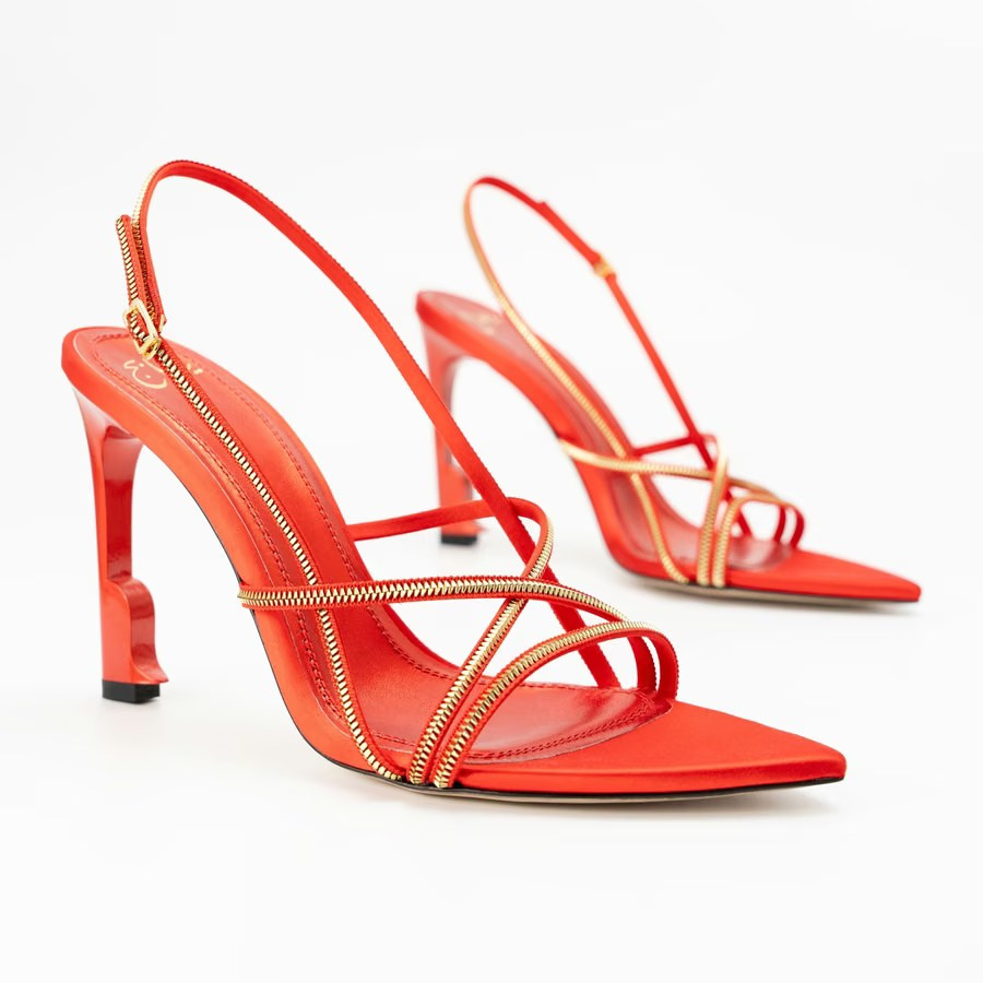 Red heeled sandals with gold zipper-style straps on a white background