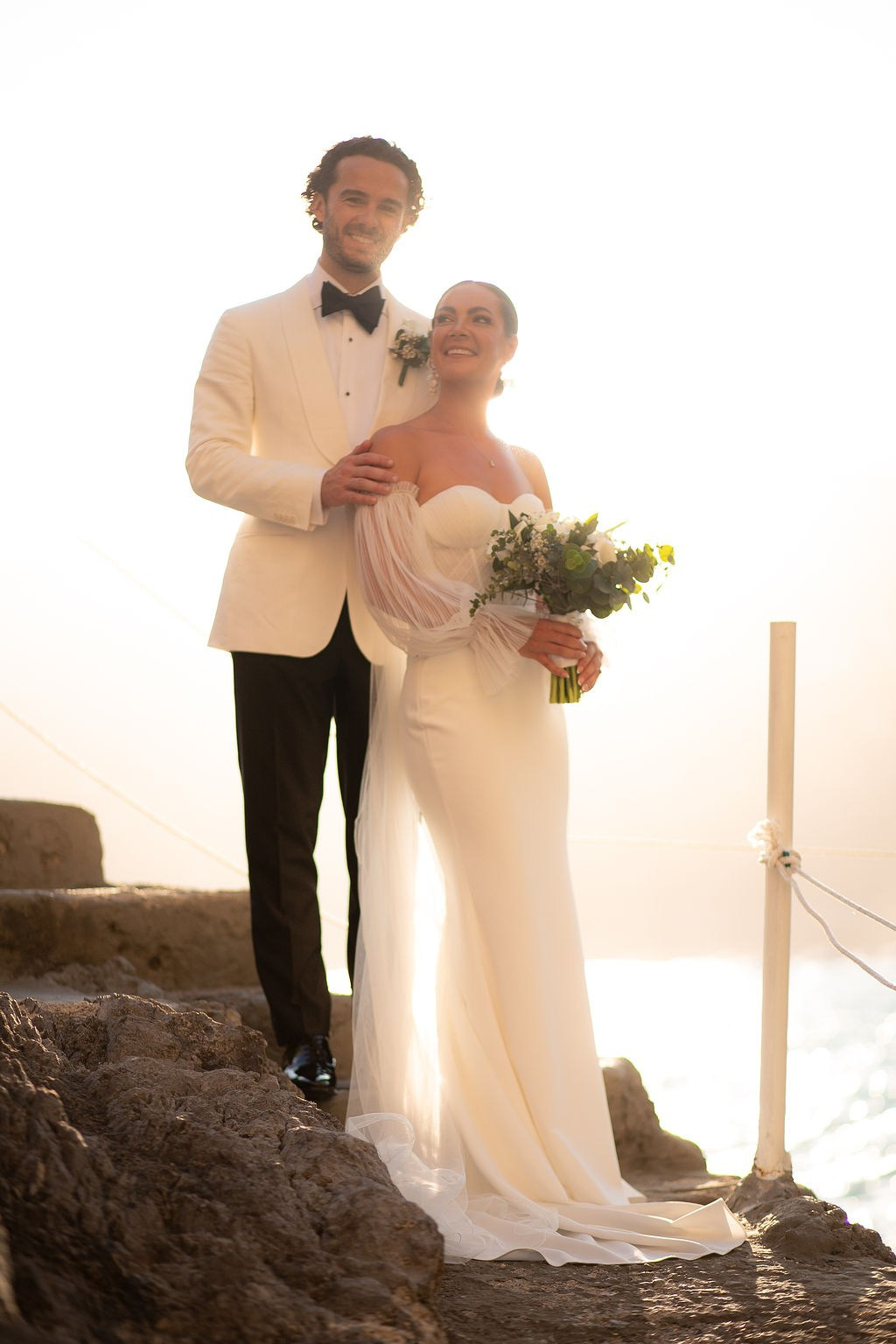 Bride and groom embracing on a cliff overlooking the Amalfi Coast at sunset