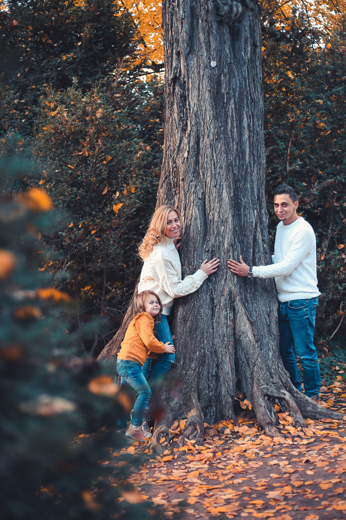 Mann im weißen Pullover und Frau im weißen Pullover und kleines Mädchen im orangenen Pullover spielen im herbstlichen Park