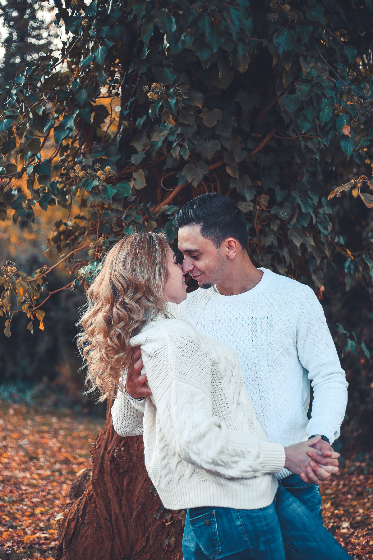 Mann im weißen Pullover und Frau im weißen Pullover kuscheln am Baum im Park