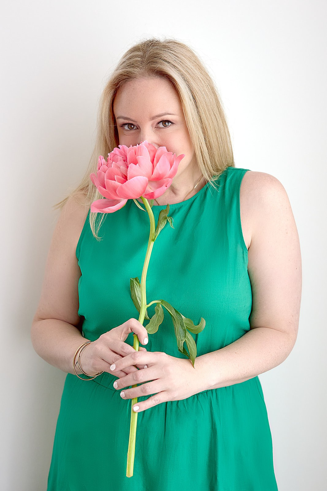 Woman in green dress sniffing a big pink flower