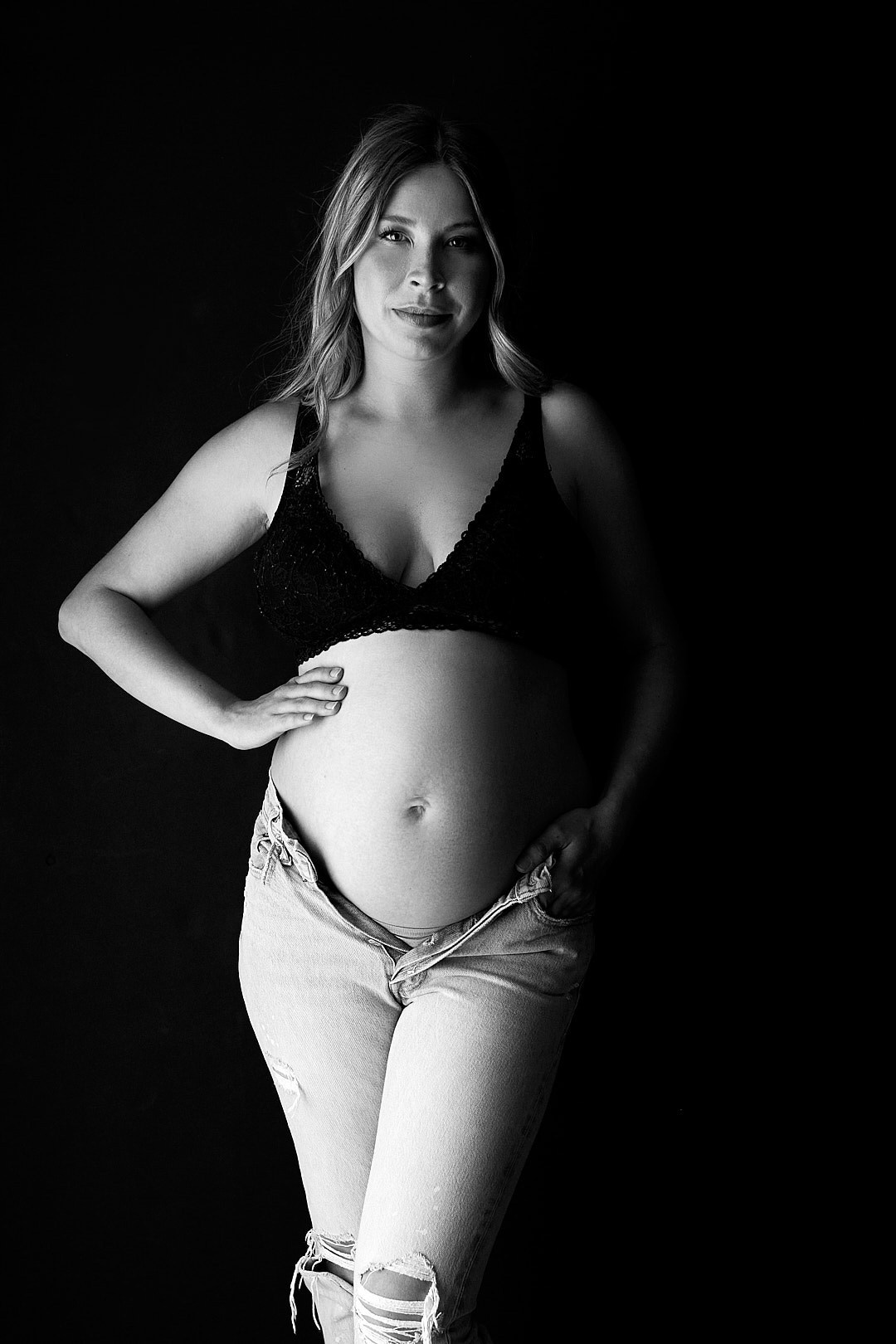 MATERNITY PHOTO OF WOMAN IN BLACK BRA AND UNDONE JEANS