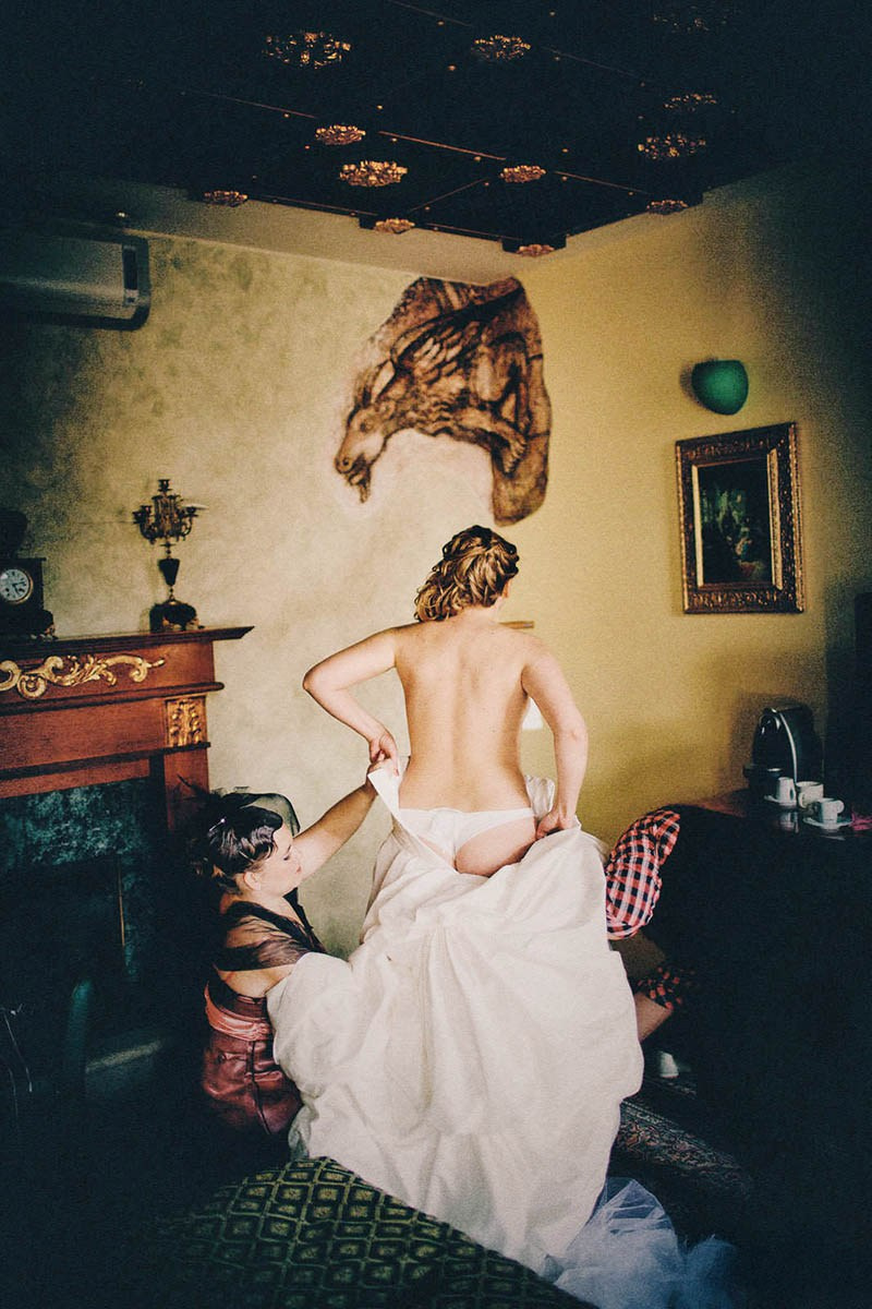 Stylishly dressed bridesmaids assist the bride as she puts on her dress in the ornate settings of the Hotel Páva in Prague.