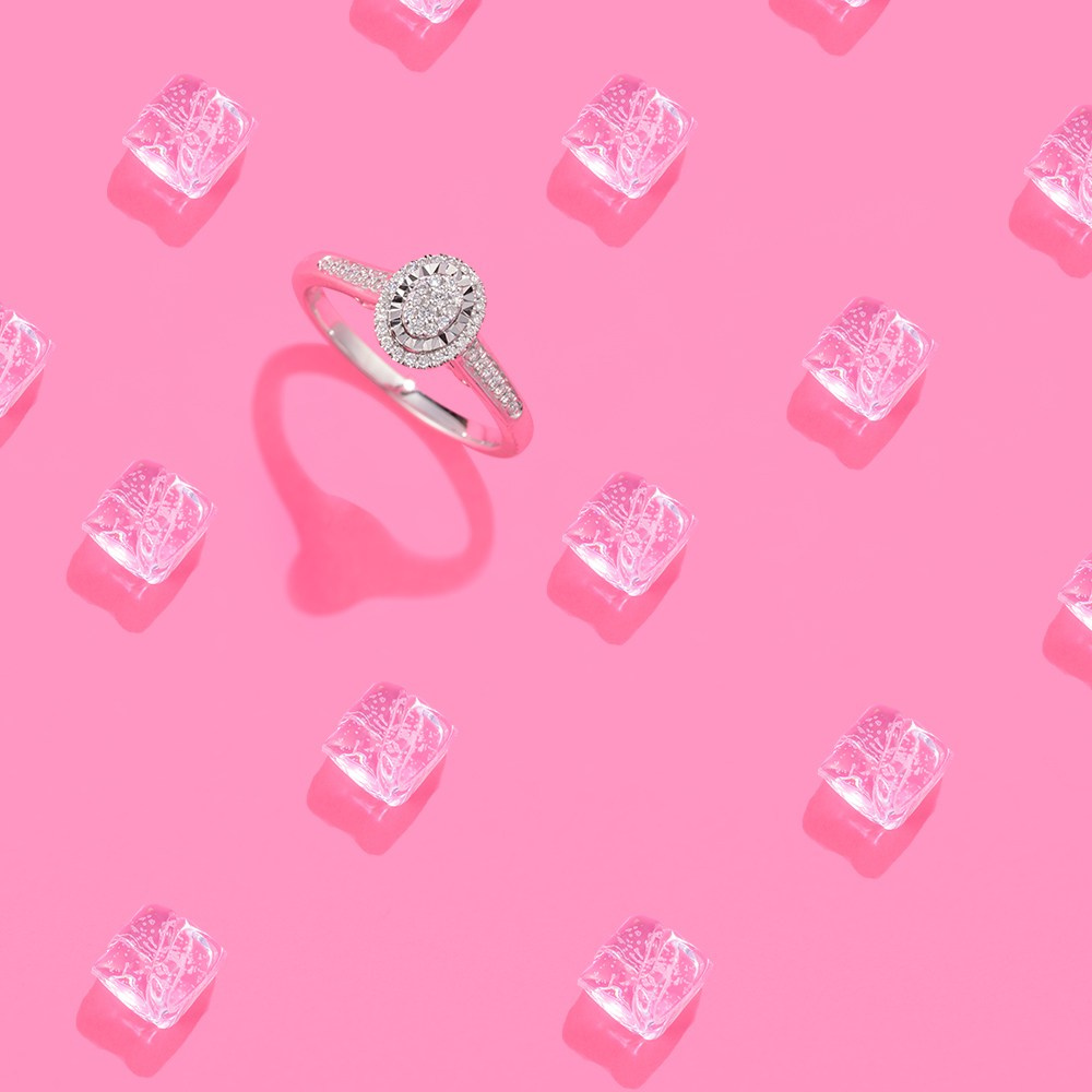 Dijamantski prsten koji stoji uspravno na roze pozadini i kockama leda.