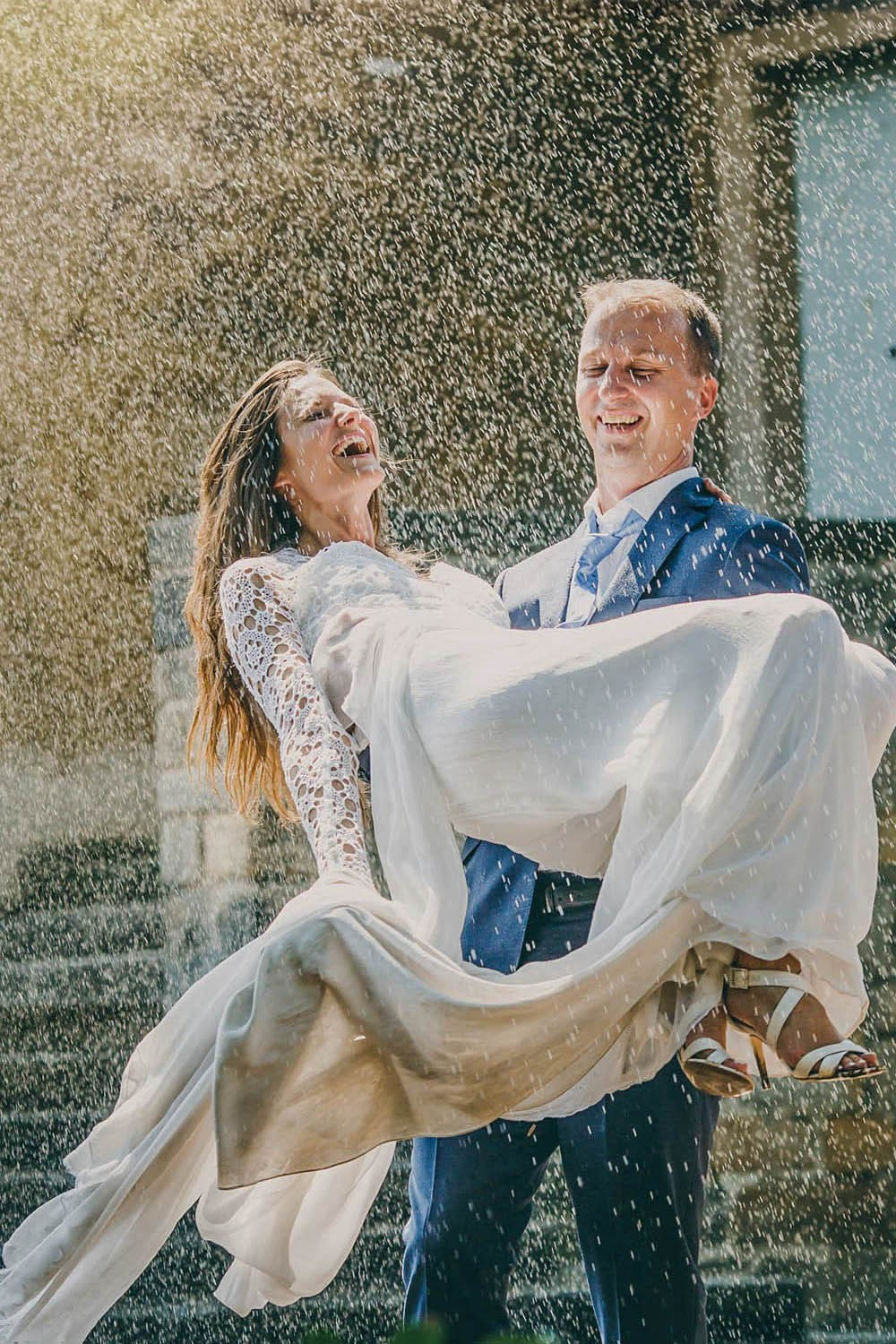 Groom carrying bride through sprinkler at Prague Castle, summer wedding