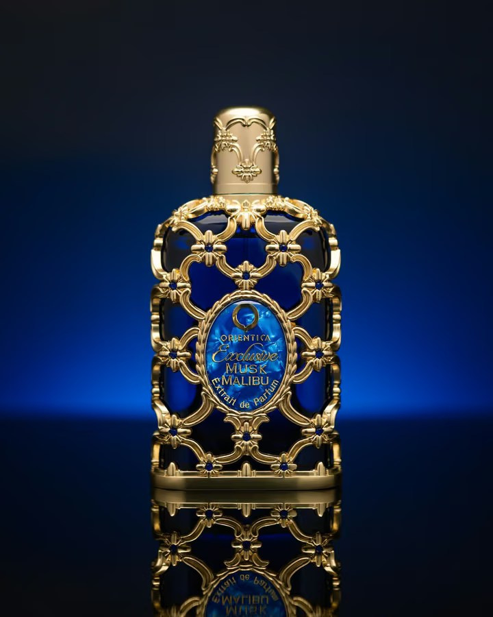 Ornate blue and gold Orientica perfume bottle reflected on a dark studio surface