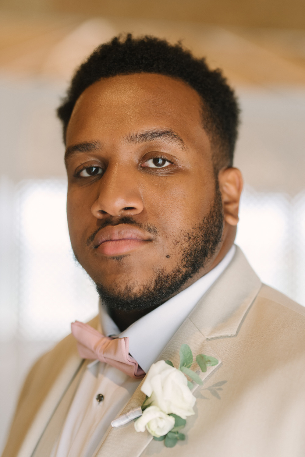 Жених смотрит в камеру. У него короткие волосы, на нем смокинг и галстук-бабочка.