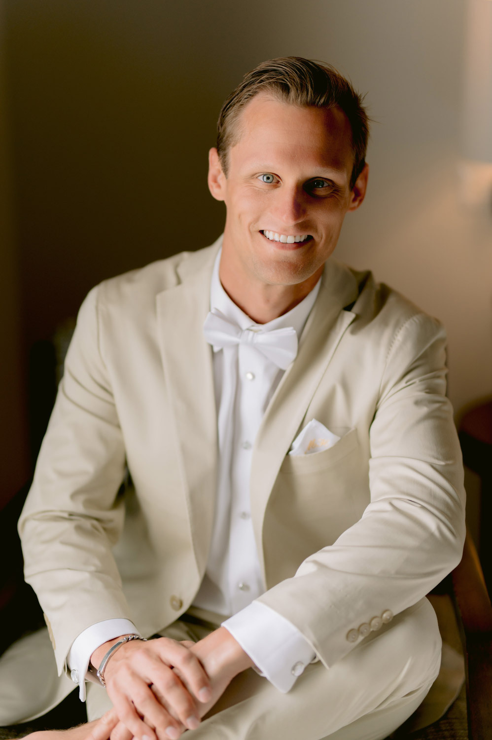 The groom poses for the photographer before the ceremony, he is dressed in a light-colored suit. 
