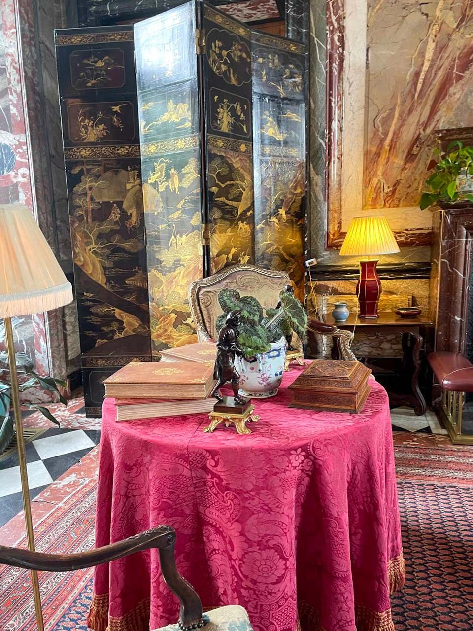 Elegant historic salon at Château de Courances featuring antique furniture, decorative screen, books and warm ambient lighting