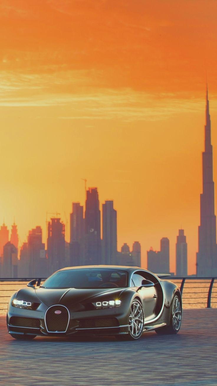 A Bugatti with Dubai skyscrapers in the background during sunset.