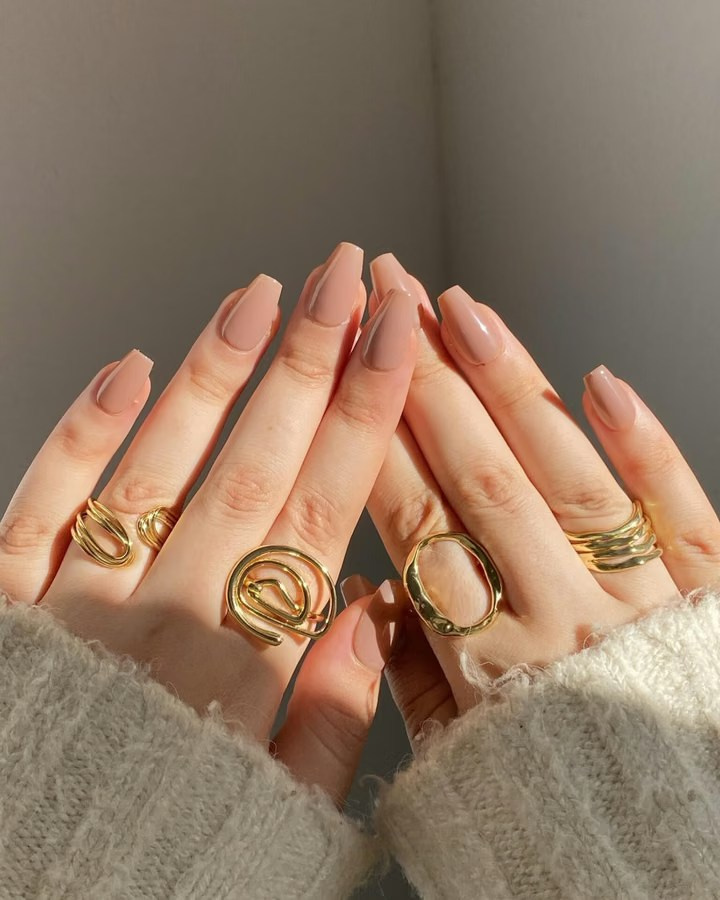 Hands wearing multiple gold rings with a neutral manicure in natural light