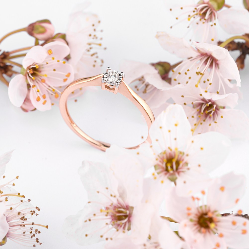 Prsten od roze zlata na beloj pozadini medju cvećem.