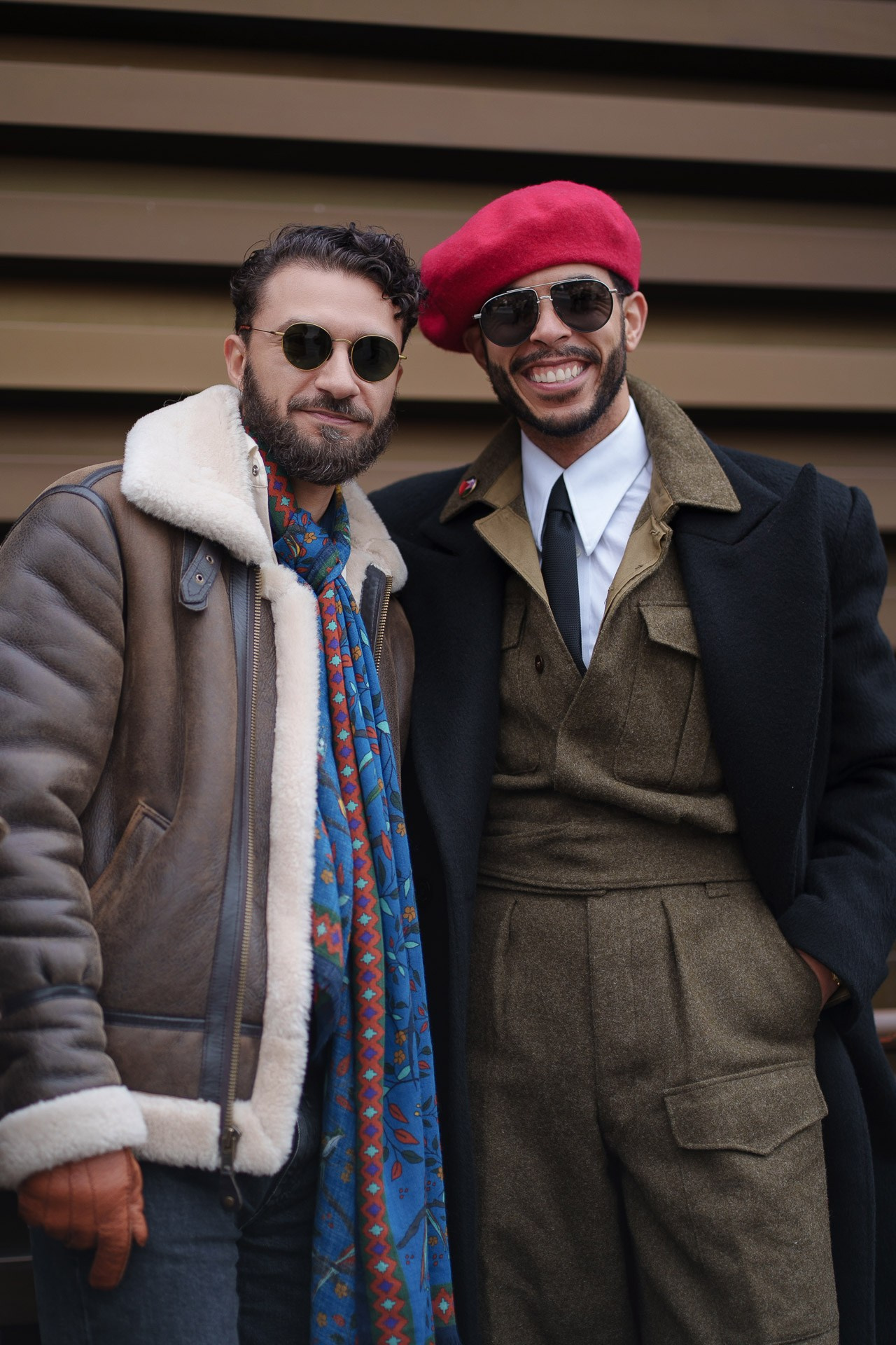 Two smiling men posing together wearing beret and tailored outfits at Pitti Uomo