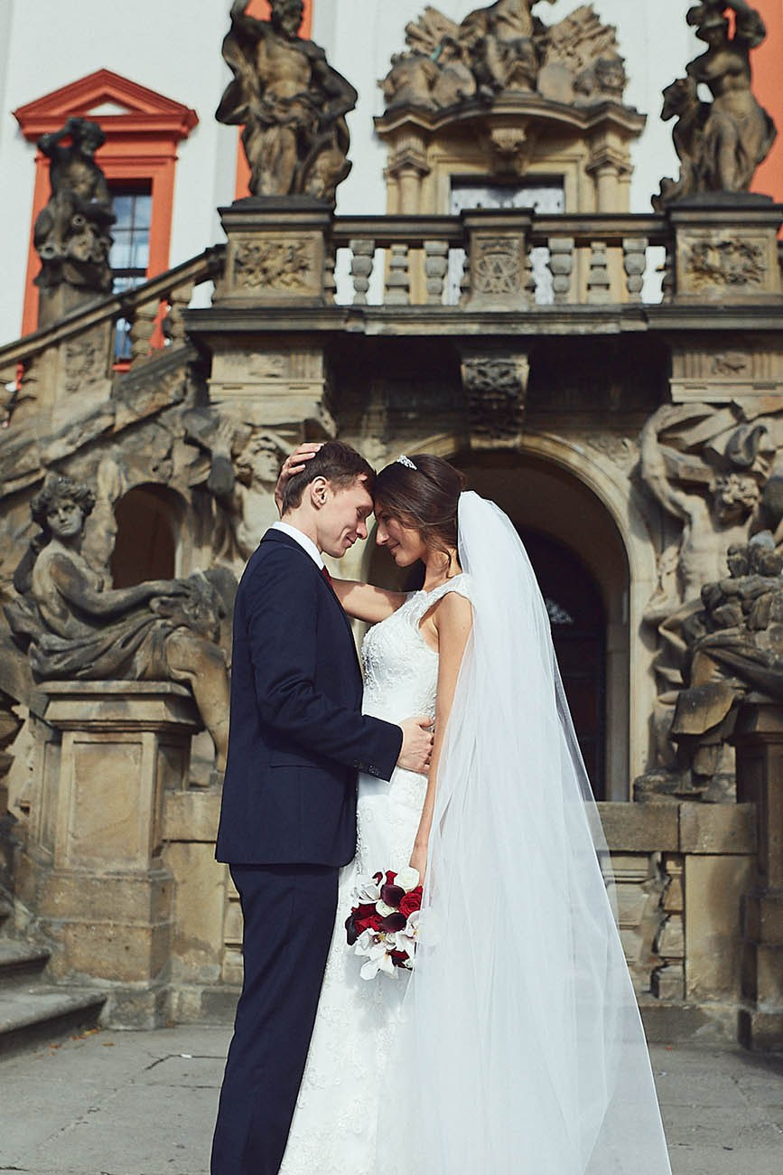 Newlyweds embrace near the historic staircase leading to the ballroom of the Troja Chateau in Prague.