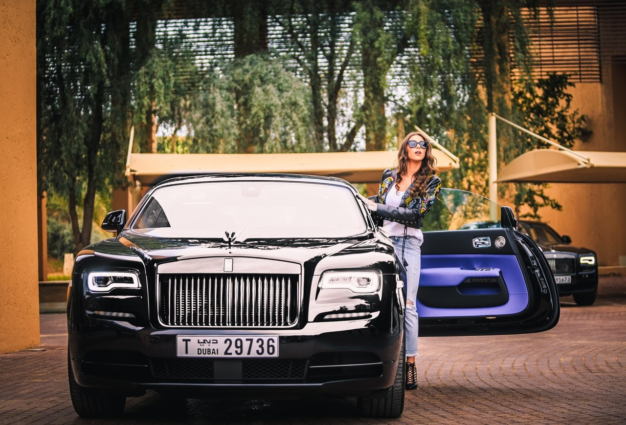  beautiful woman in jeans and sunglasses stands next to a black Rolls-Royce in Dubai