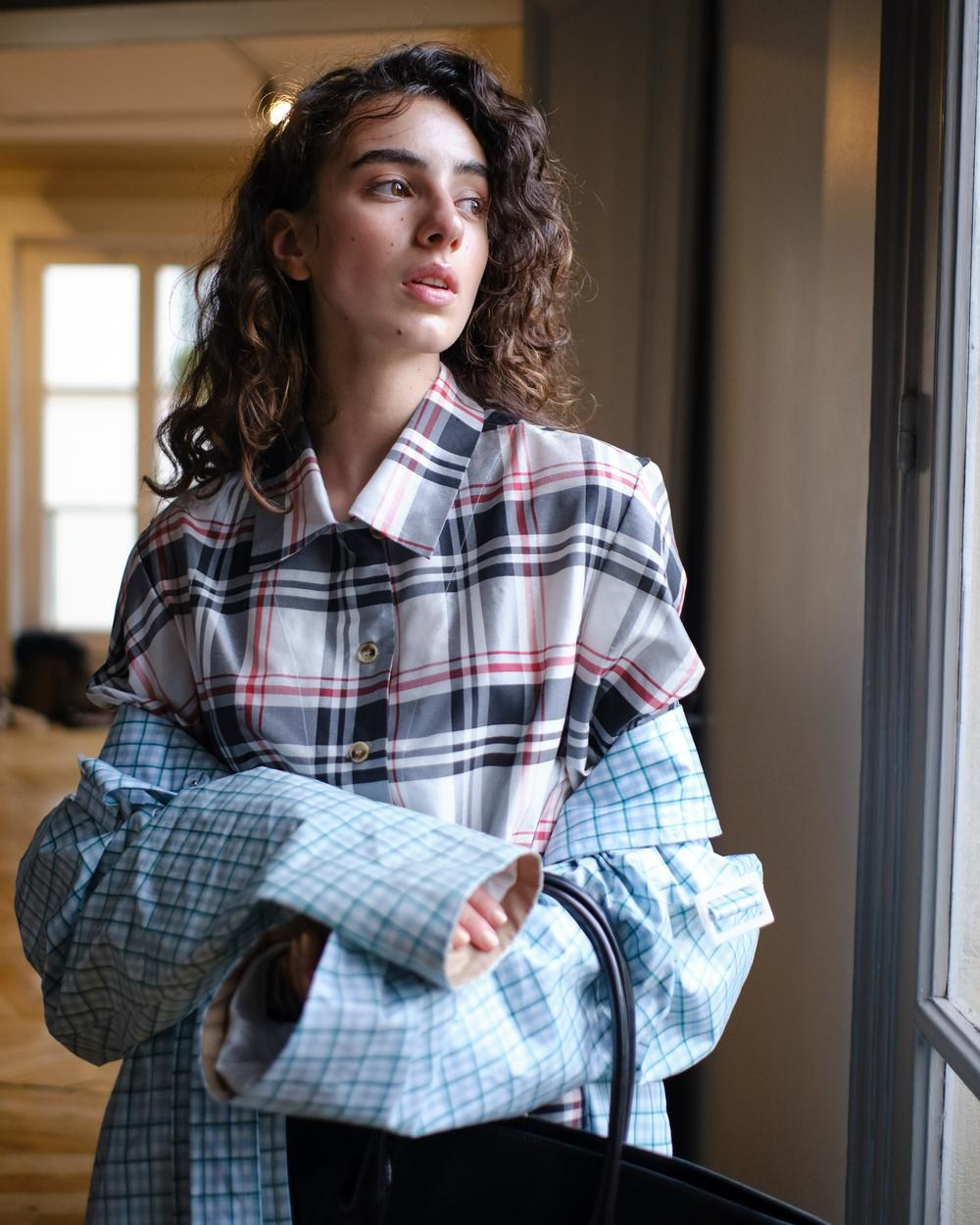 Commercial casual lookbook look with a plaid shirt and oversized blue coat by a window