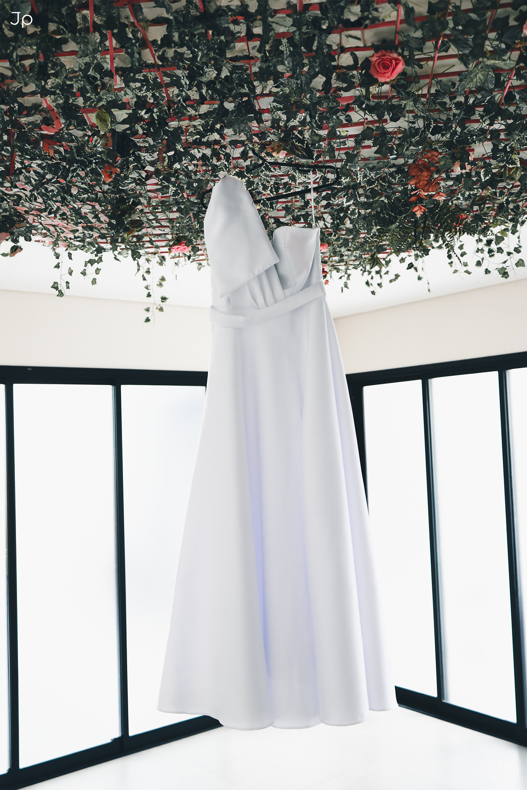 Cortina branca fluida iluminada por luz natural suave e um vestido de noiva pendurado.