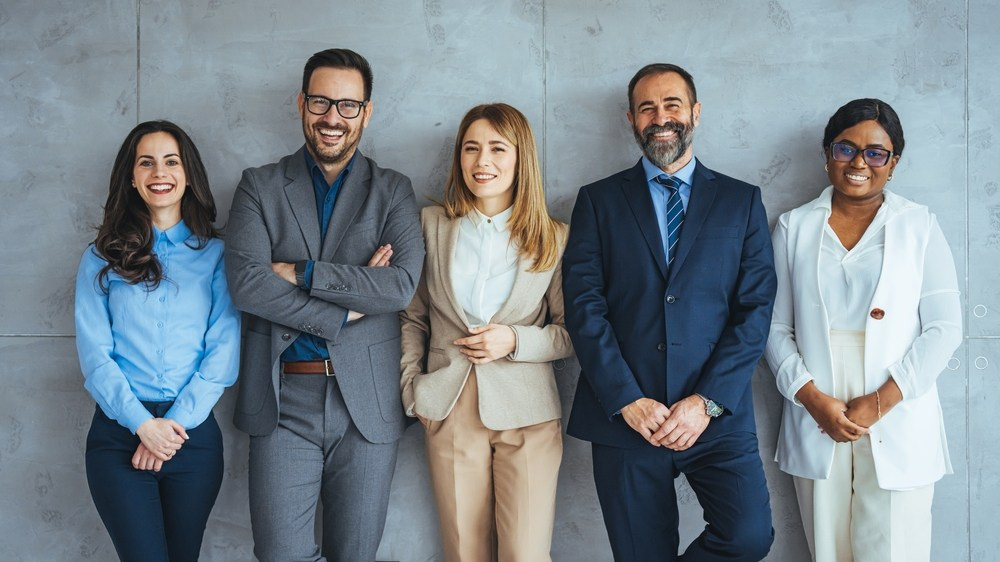 Corporate team portrait featuring three men and two women in business attire, all smiling confidently