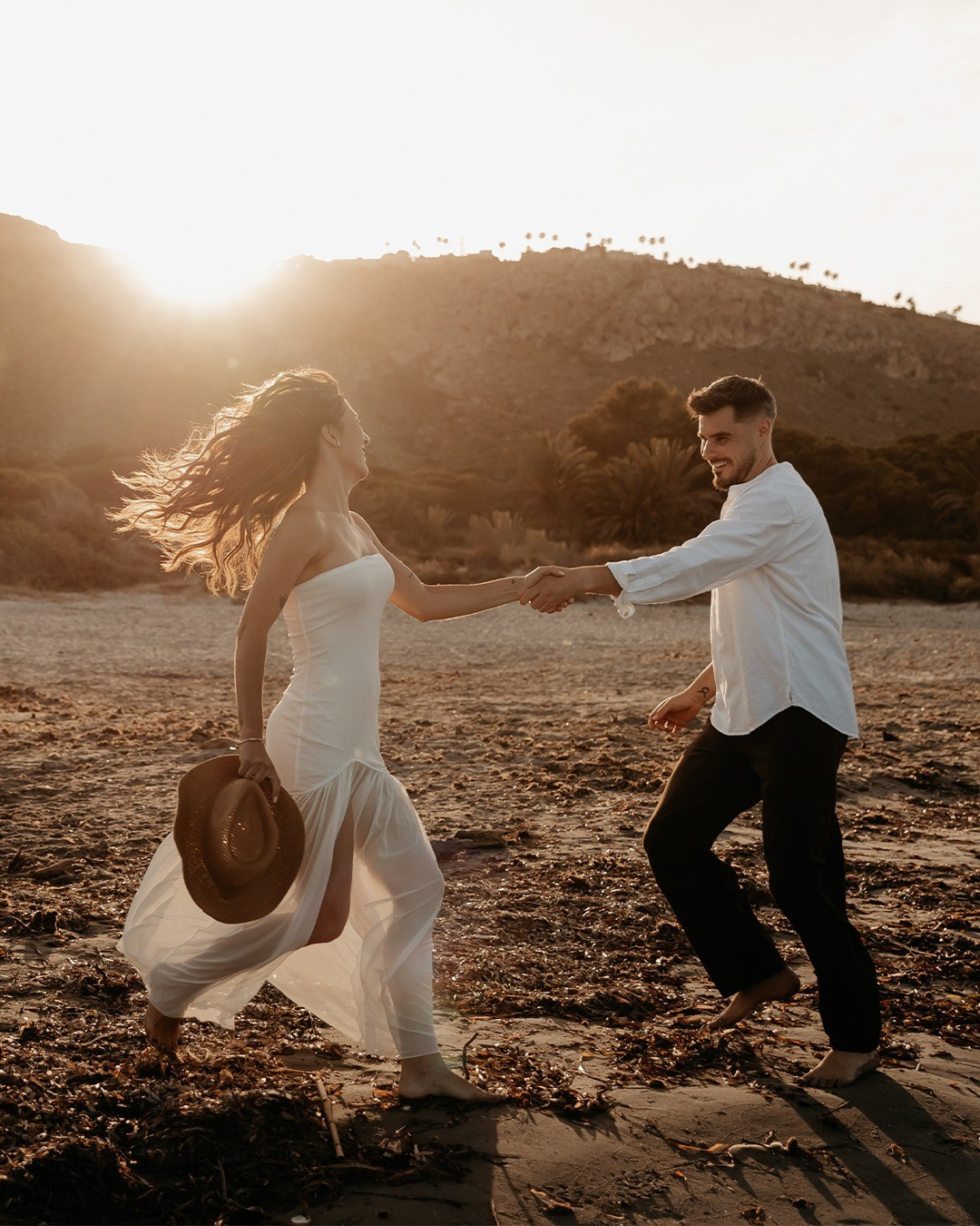 Pareja corriendo de la mano durante una sesión de fotos al atardecer.