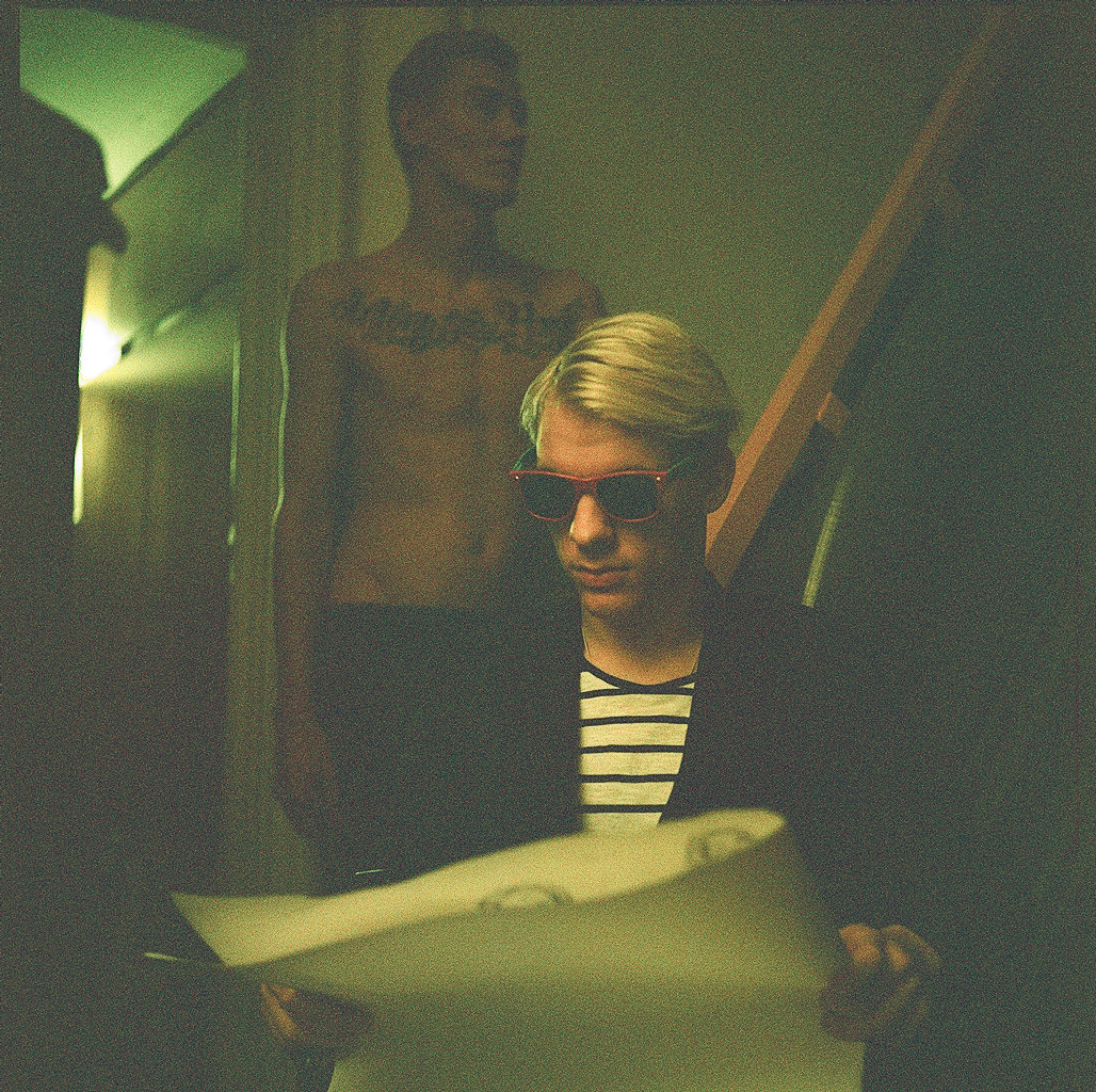 Porträt eines Mannes mit Sonnenbrille, der im Rollstuhl sitzt und eine Zeitung liest, während im Hintergrund ein barbusiger Mann sitzt,  wheeling heart Projekt  