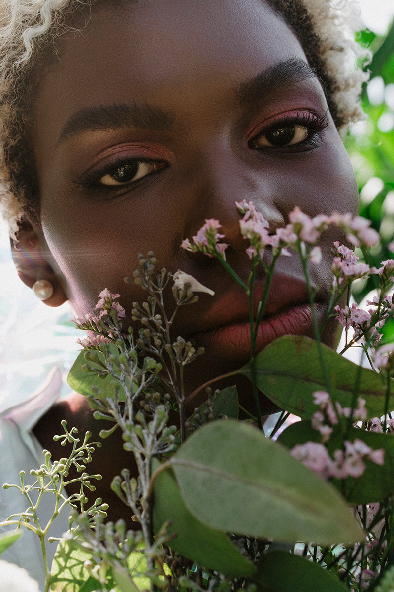 Nahaufnahme Porträt Frau schaut über Pflanzen mit rosa Make-up in die Kamera