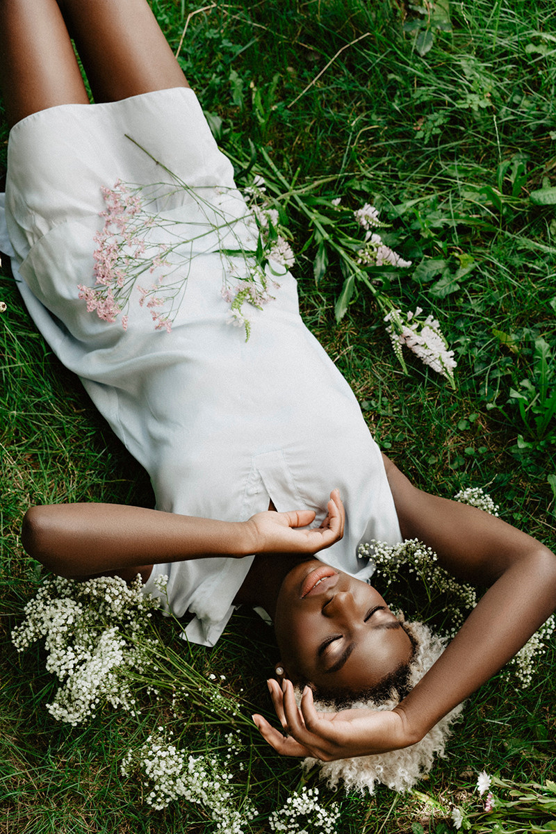 Ganzkörperporträt Mädchen liegt im Gras mit hellblauem Kleid und Armen vor dem Gesicht