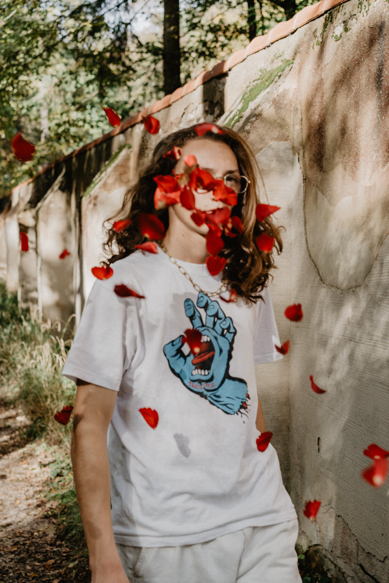 ein junger Teenager geht auf der Straße mit Rosen, die auf seinen Weg fallen und sein Gesicht bedecken, veröffentlicht in Vogue