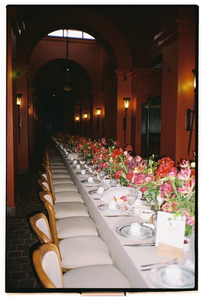 Long reception table with red florals in historic wedding corridor