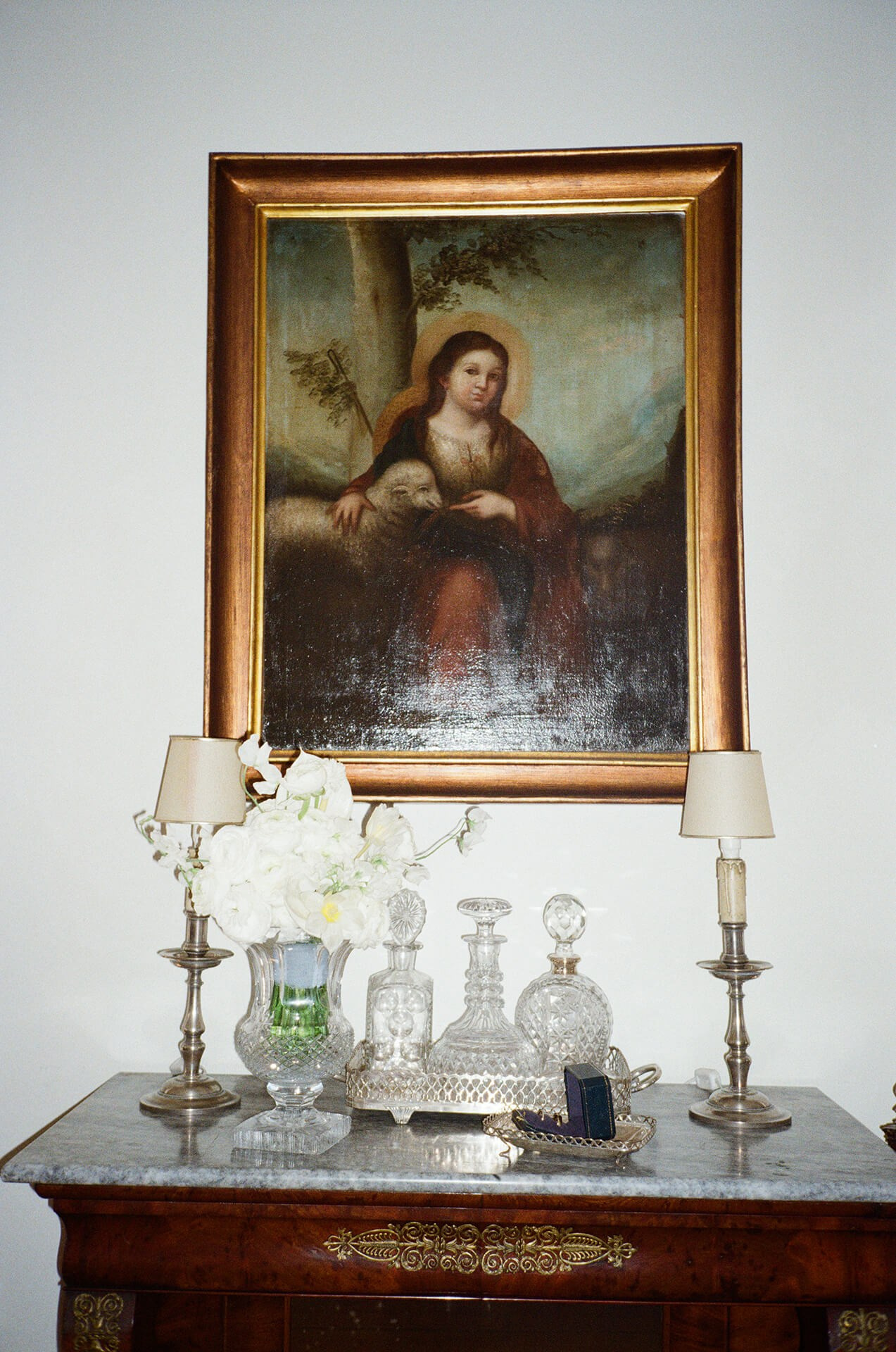 Vintage oil painting next to white wedding flowers and crystal decanters on a sideboard, interior detail at Portugal wedding