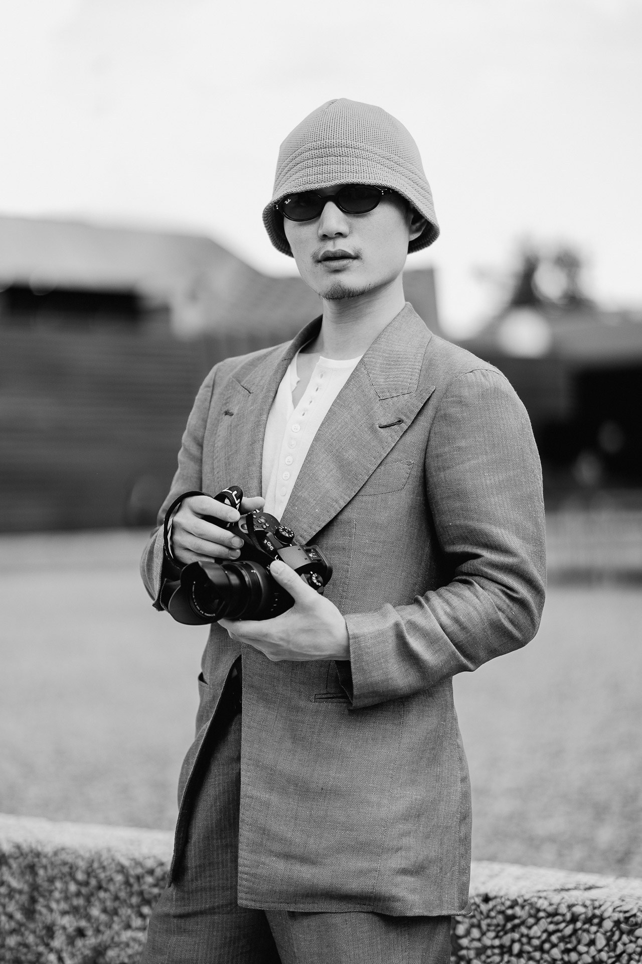 Black and white portrait from Pitti Uomo 110, guest in suit and bucket hat holding a camera