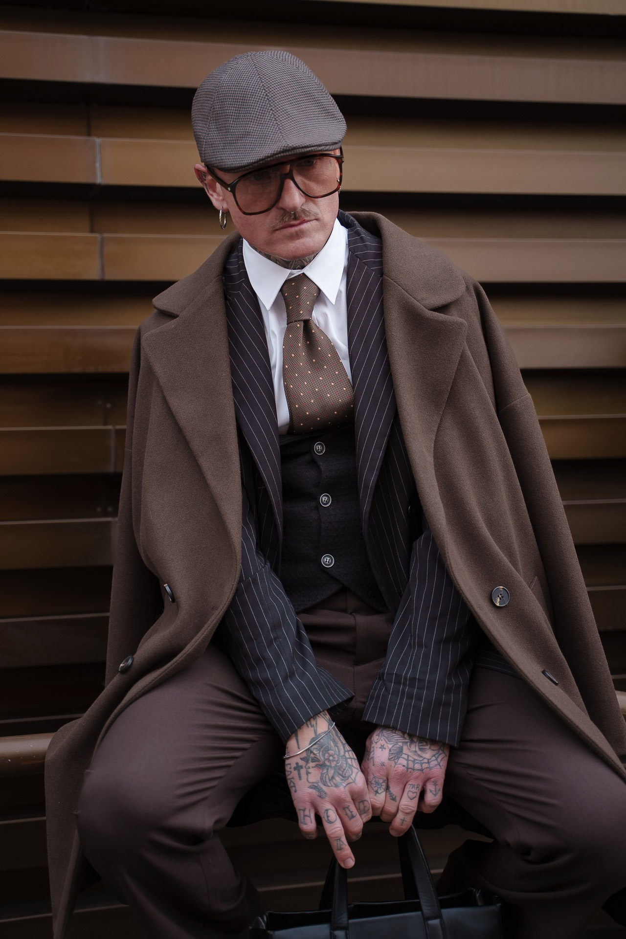 Man in brown overcoat and flat cap sitting at Pitti Uomo 109 Florence