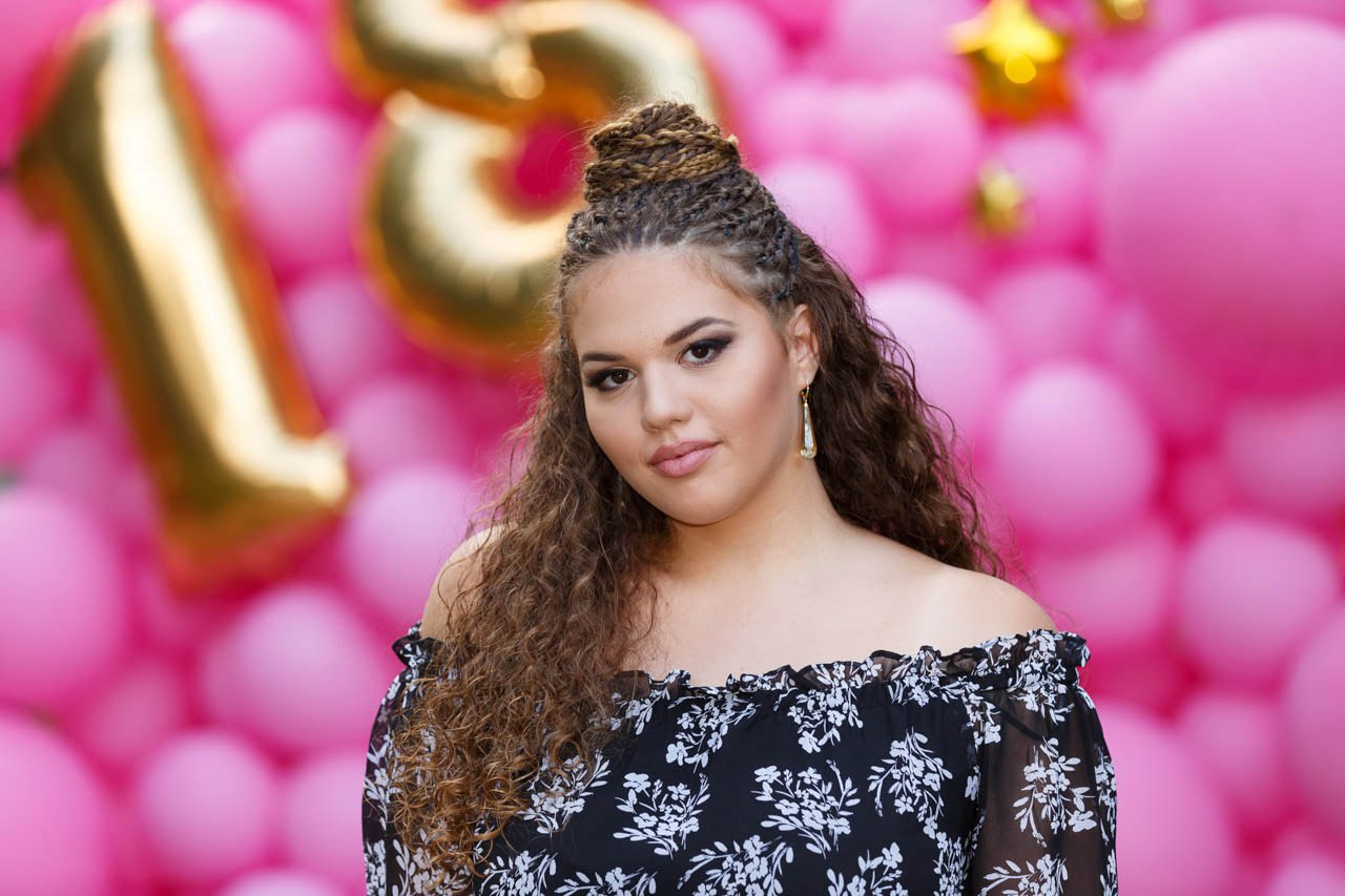 Devojka u elegantnoj haljini pozira ispred dekoracije za 18. rođendan.