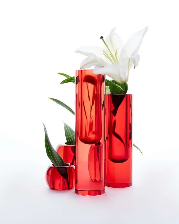 Red glass vases with green leaves and a white lily on a clean studio background
