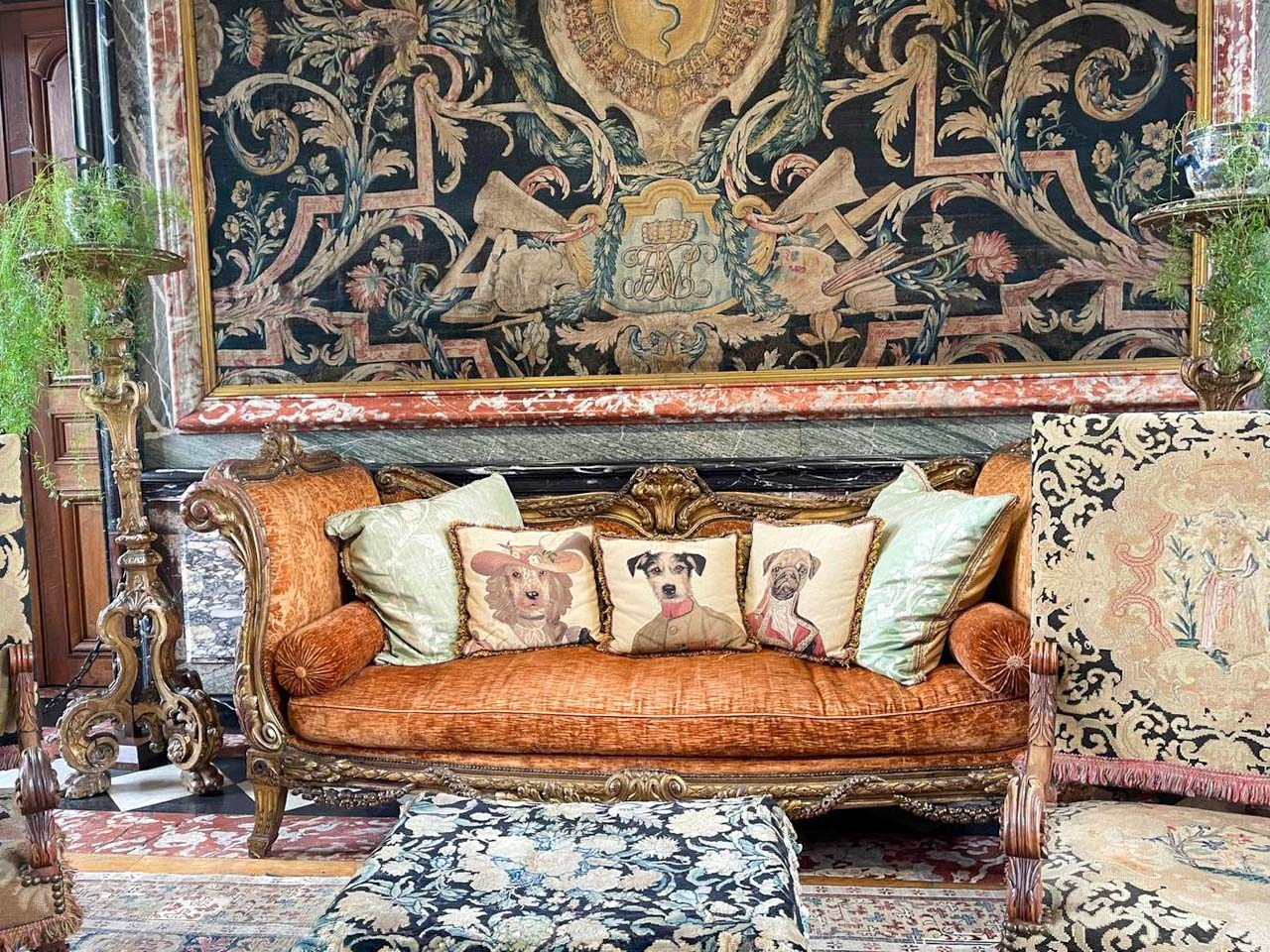 Ornate antique sofa beneath a historic tapestry at Château de Courances, decorated with elegant dog-themed cushions