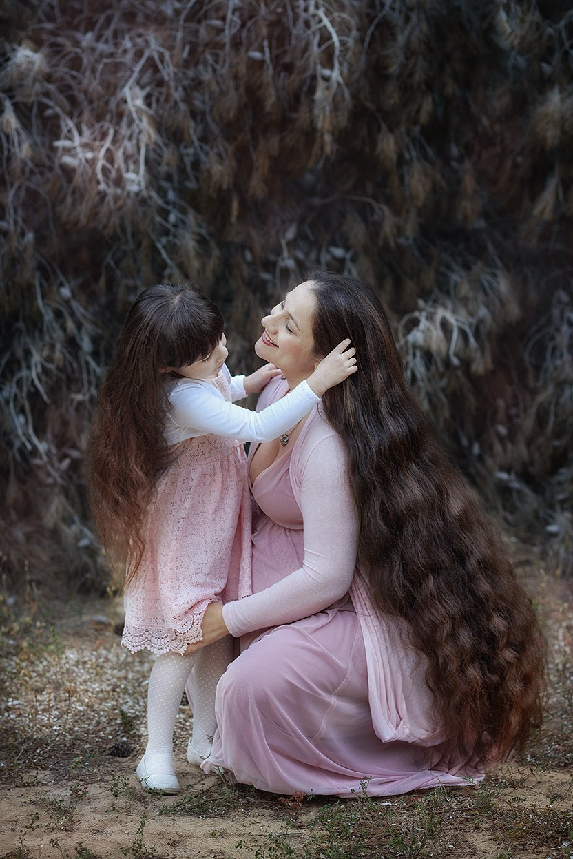 Mother and daughter with long hair in the forest, looking at each other with love.