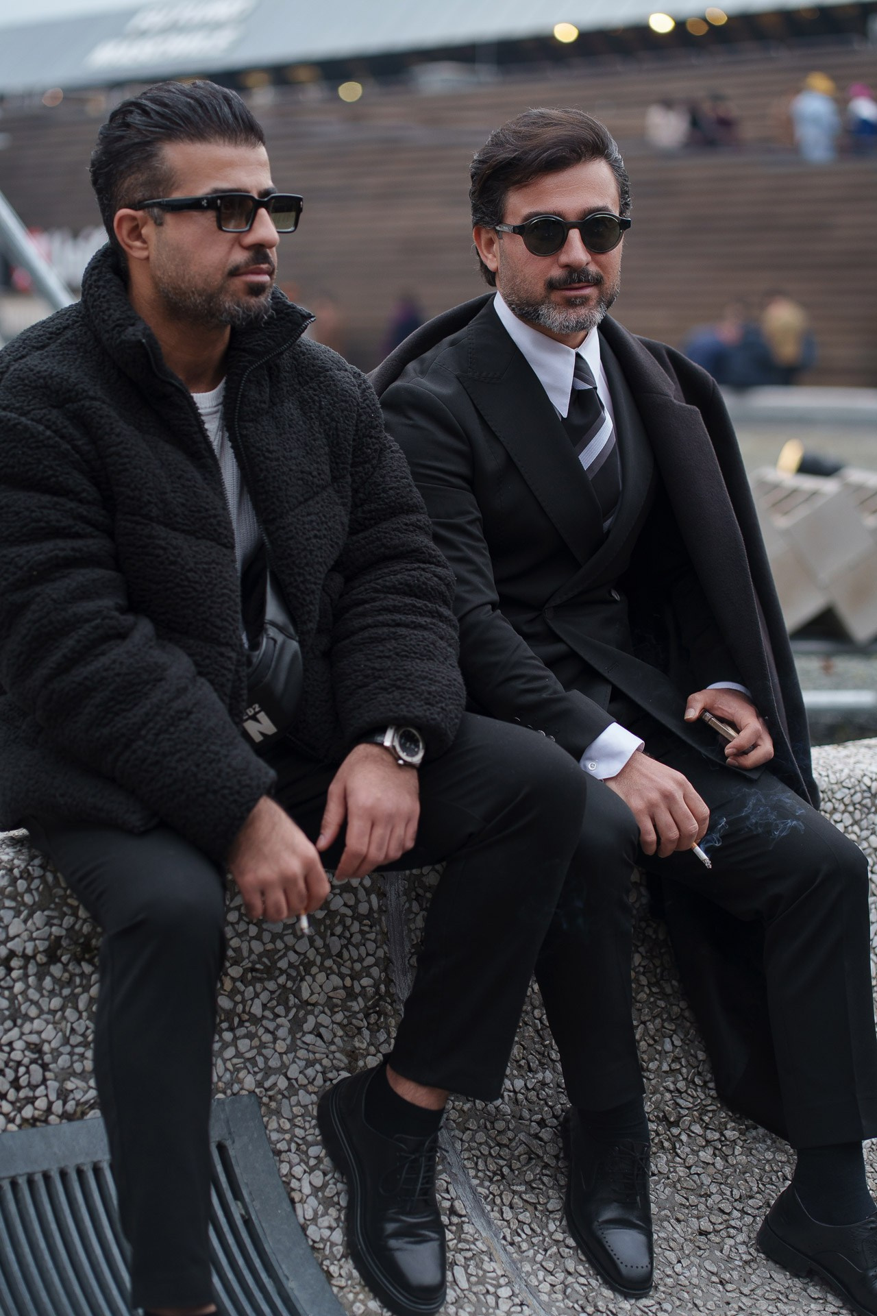 Two stylish men in black coats sitting together at Pitti Uomo 109 Florence