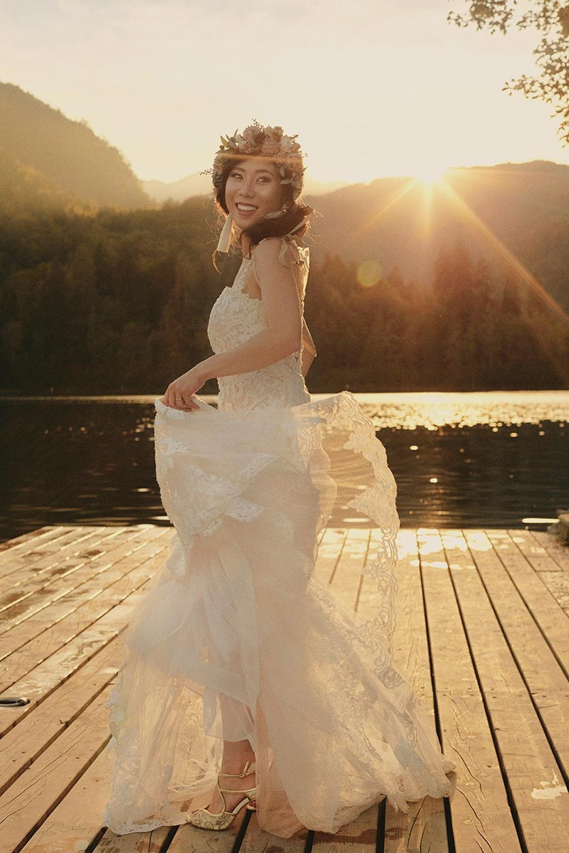 Radiant Asian bride with floral headpiece twirls in her wedding dress as the golden flare from the sun beautifully illuminates her.