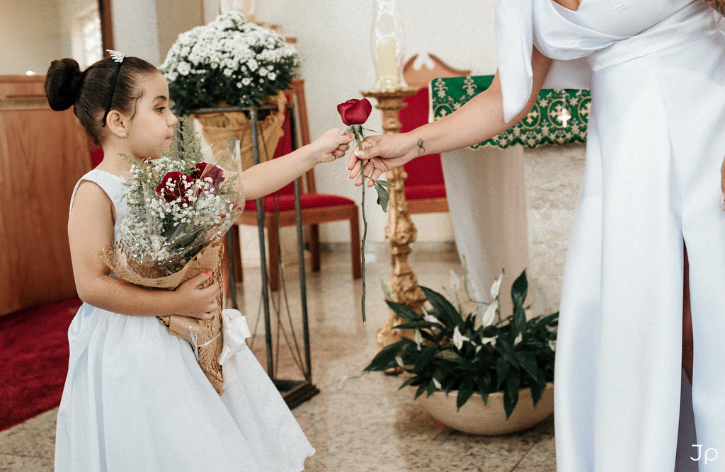 Noiva pega um botão de rosas com a daminha.