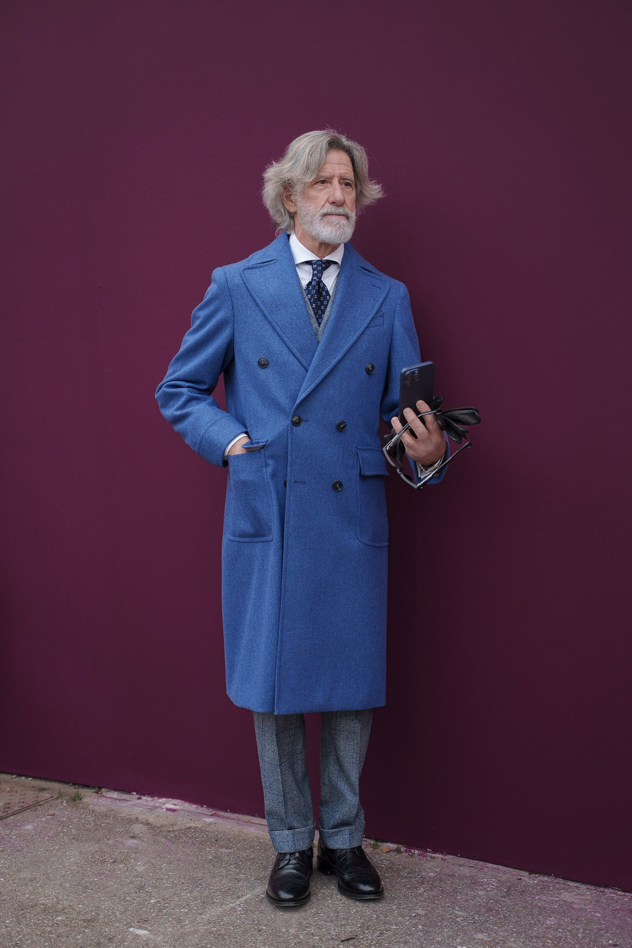 Older man in blue double breasted coat posing against purple wall at Pitti Uomo 109