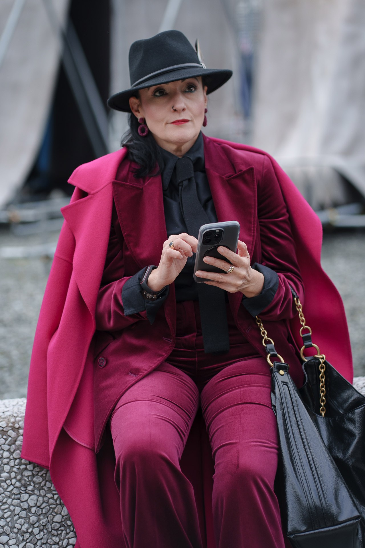 Elegant woman in burgundy suit and black fedora using phone at Pitti Uomo 109 Florence