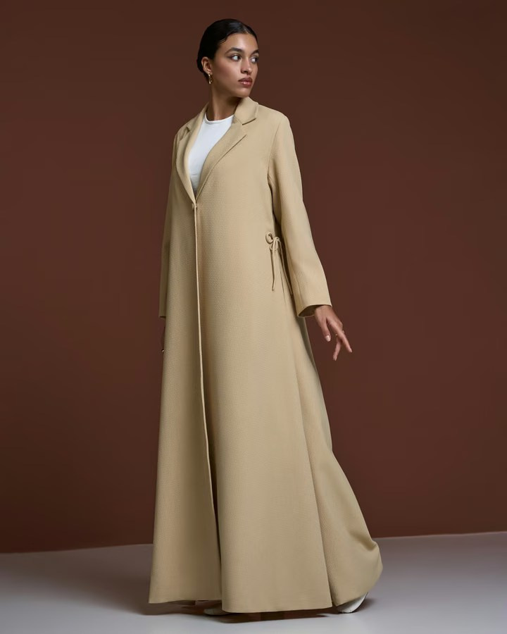 Model wearing a flowing beige coat in a minimalist studio lookbook