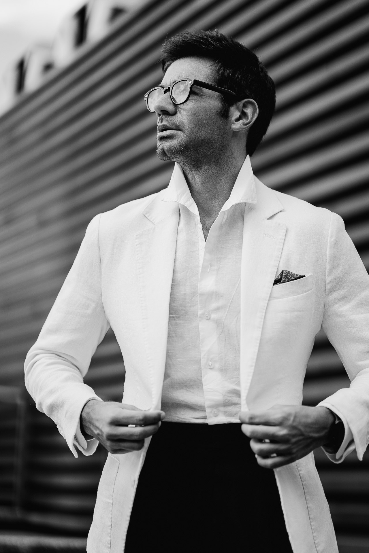 Black and white Pitti Uomo 110 portrait, man adjusting white blazer outside Fortezza da Basso