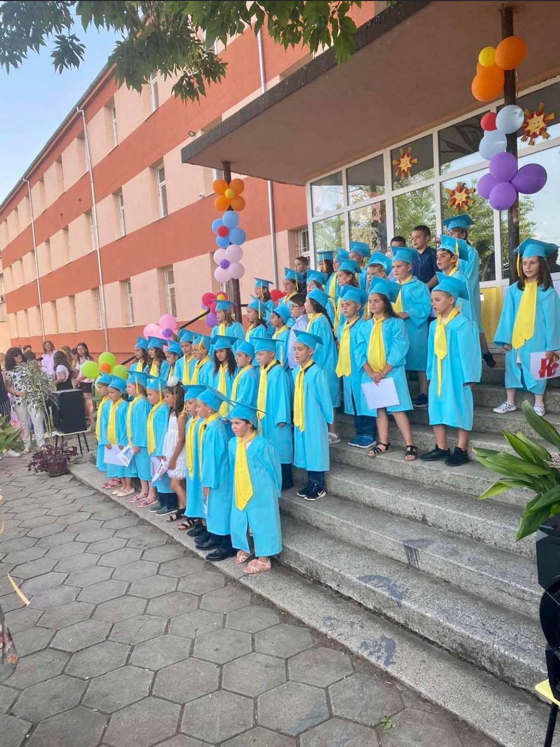 деца с детски тоги и академични шапки завършват първи клас 