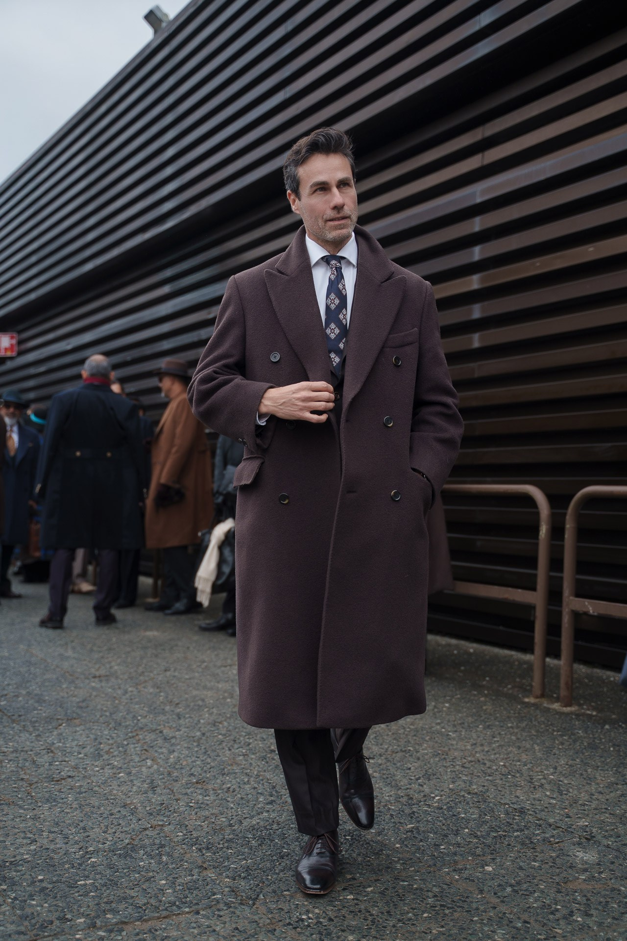 Man in brown double breasted coat and tie walking outside Pitti Uomo 109 Florence