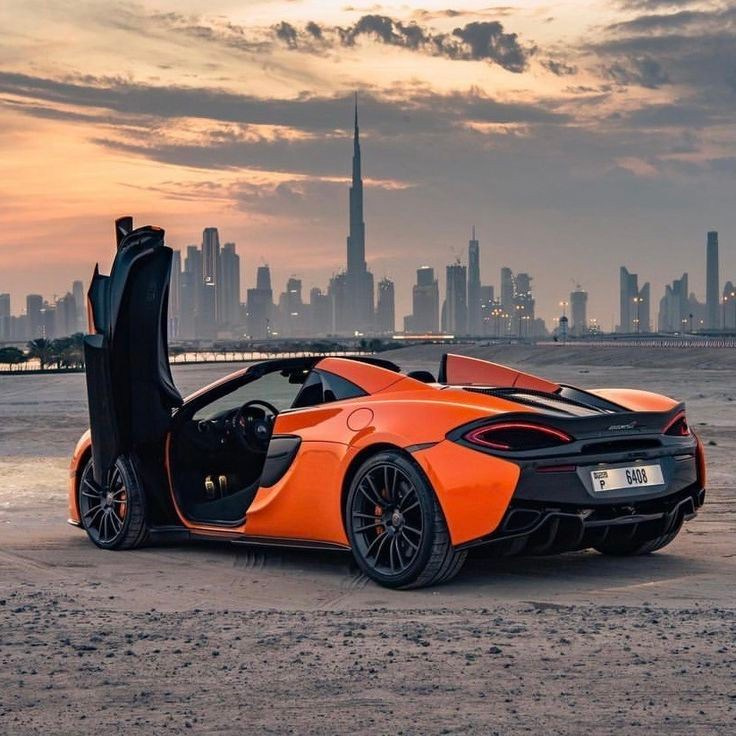 An orange McLaren with Burj Khalifa and Dubai landscapes under a beautiful sky.