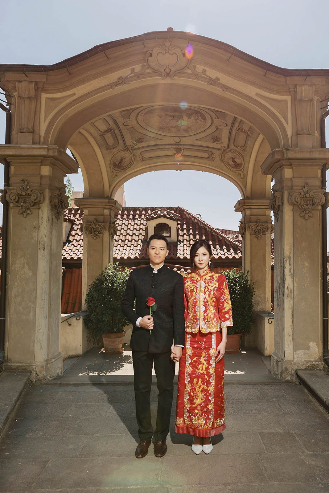Taiwan couple in traditional Chinese wedding attire posing with a red rose in the Ledebour Garden in Prague.